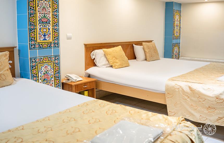 اتاقی در هتل «ملک» اصفهان که دو تخت در آن است، ستون‌های کاشی‌کاری‌شده دارد و دیوارهایش سفیدرنگ است.